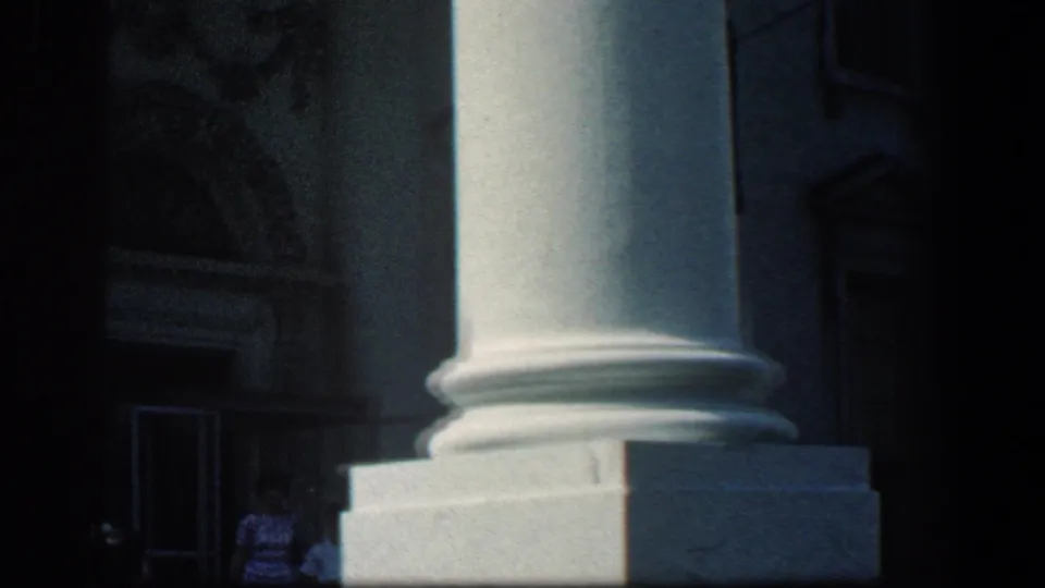 1961 Baltimore frame of tall classical columns and a recessed doorway, with a small indistinct person near the entrance.