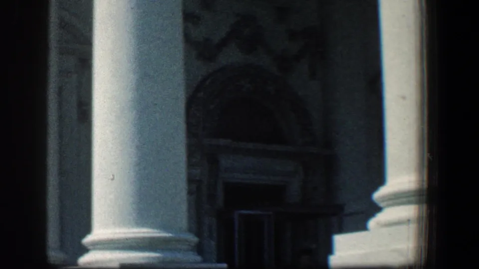 1961 Baltimore home-movie frame showing column bases, arched architectural trim, and a shadowed doorway on a civic-looking facade.
