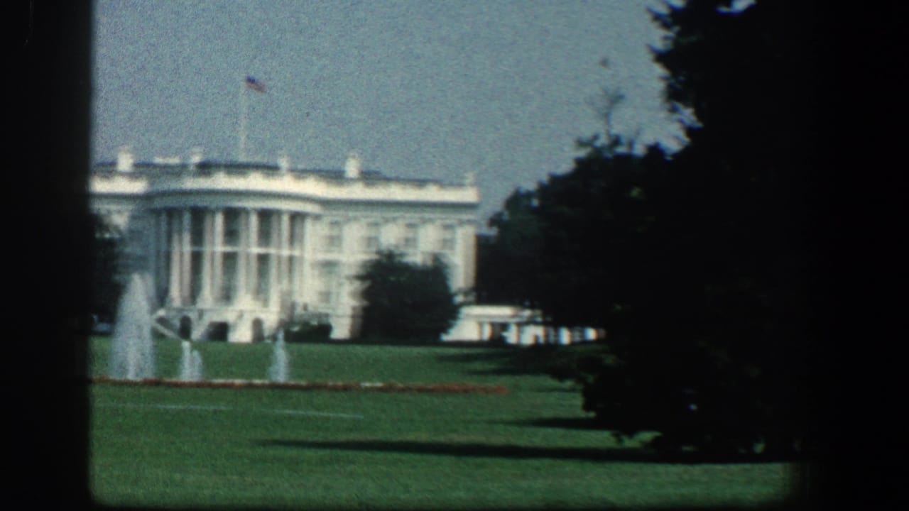 White House seen across lawn and fountains with trees framing the view.