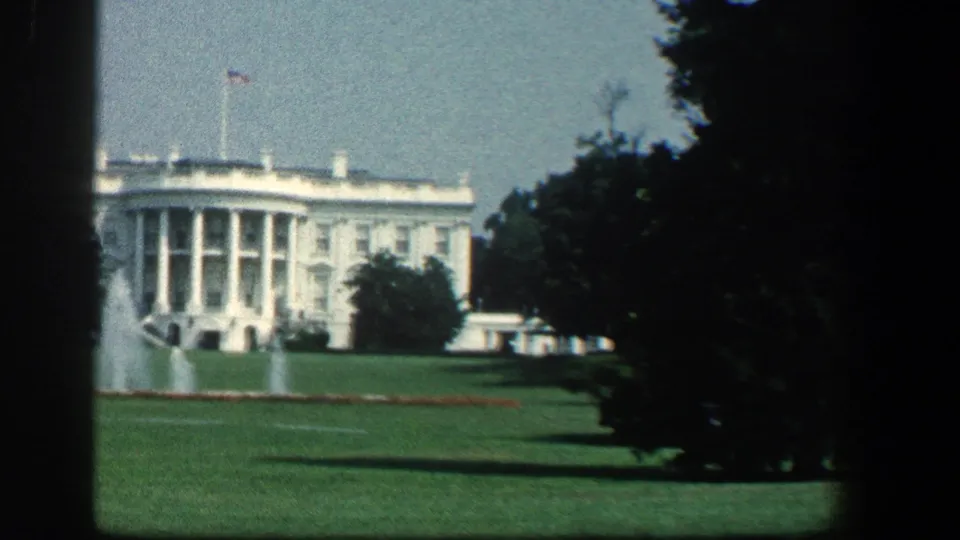 1961 8mm frame showing the White House, lawn fountains, flagpole, and a dark gate-like border from the film frame.