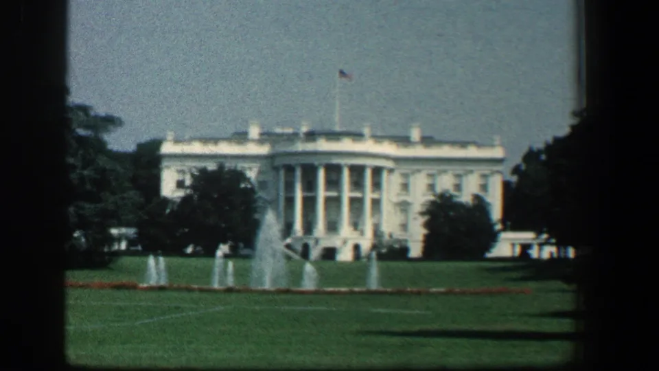 1961 8mm view of the White House centered behind South Lawn fountains, with trees, flag, and soft home-movie color.