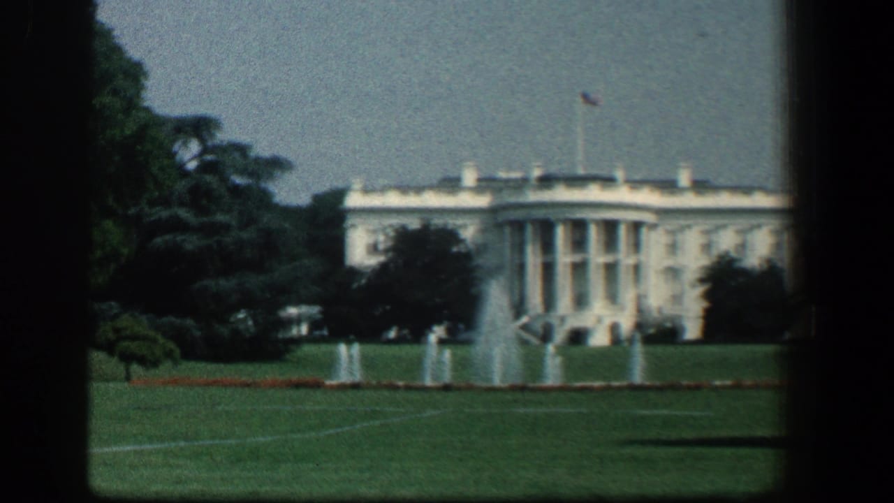 1961 8mm view of the White House across the lawn, with fountains, trees, flagpole, and soft home-movie focus.