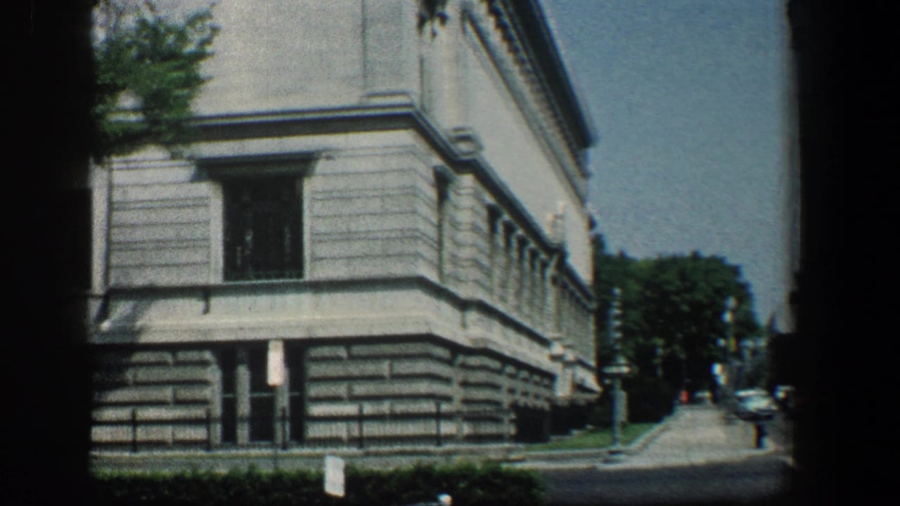 Similar street view of the building corner with sidewalk, trees, and distant cars.