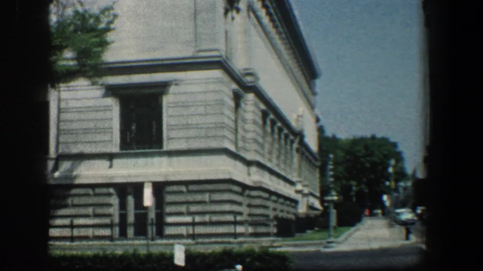 1961 Baltimore view of the institutional building corner from the street, with masonry details, trees, sidewalk, and parked cars beyond.