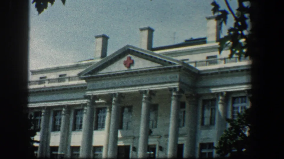 1961 Baltimore exterior of the Red Cross-marked hospital building, showing columns, pediment, windows, and tree shadows.