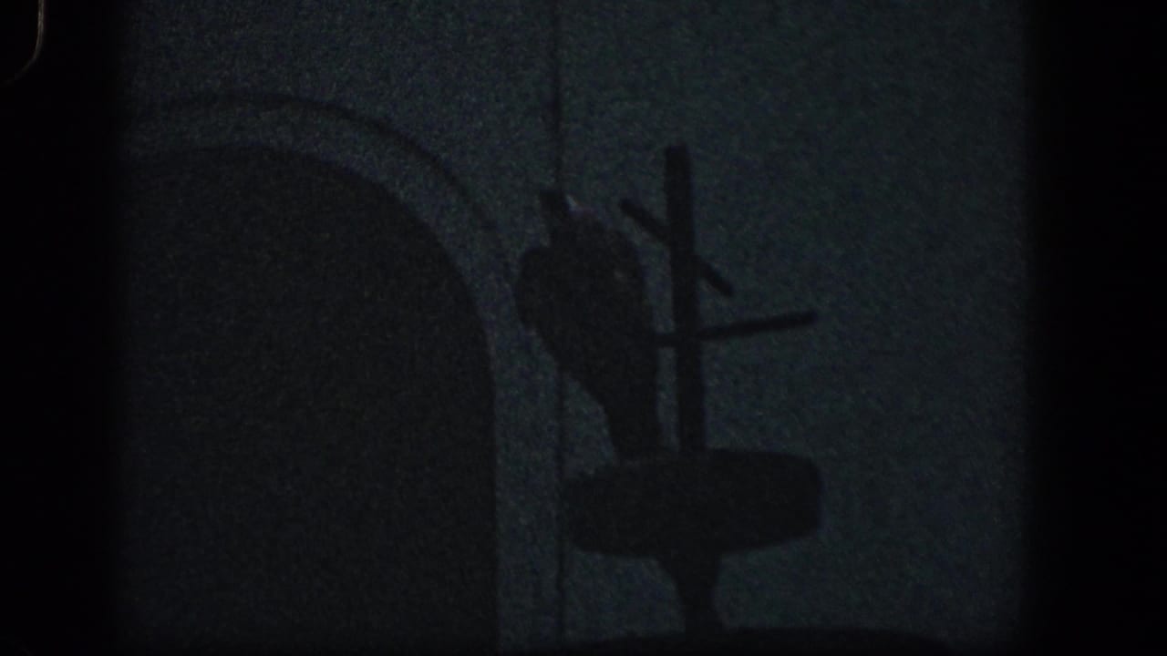 1961 Baltimore 8mm frame showing dark outdoor storm debris, an arched form, and a cross-shaped silhouette against a dim sky.