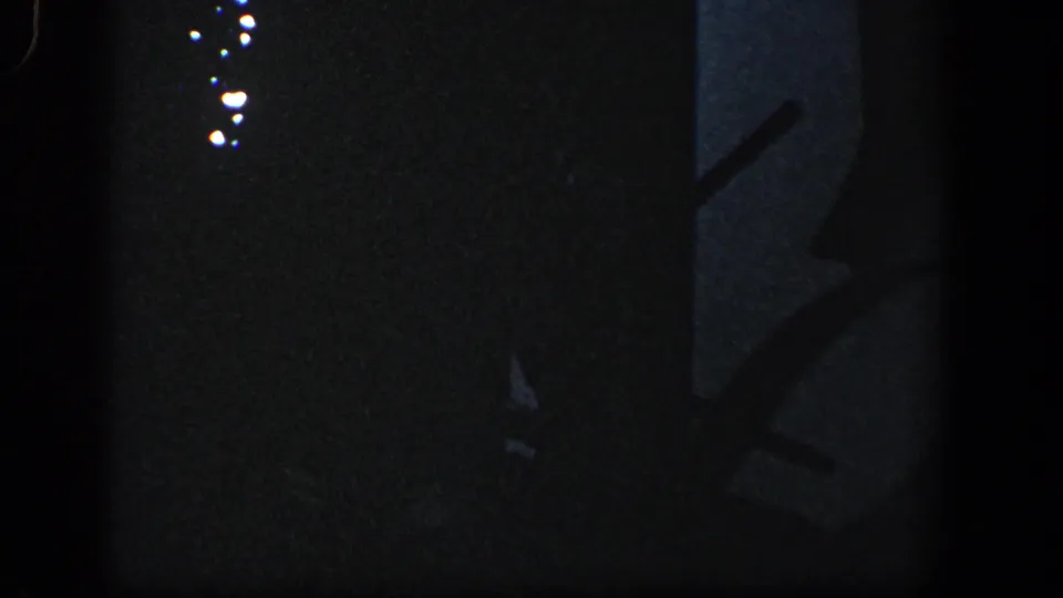 Grainy 8mm frame from the Baltimore storm aftermath showing silhouetted damaged pieces and small bright light spots in deep shadow.
