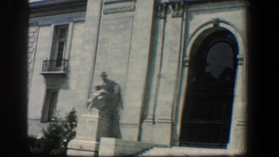 1961 Baltimore 8mm frame showing a pale stone facade, arched doorway, pedestal statue, and upper window with a small balcony.