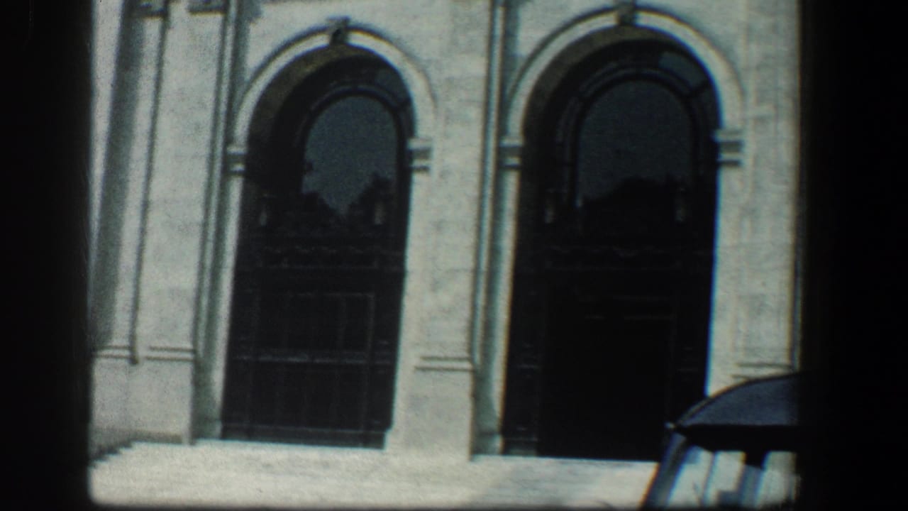 Two dark arched entrances in a pale stone building, with part of a car at the lower right.