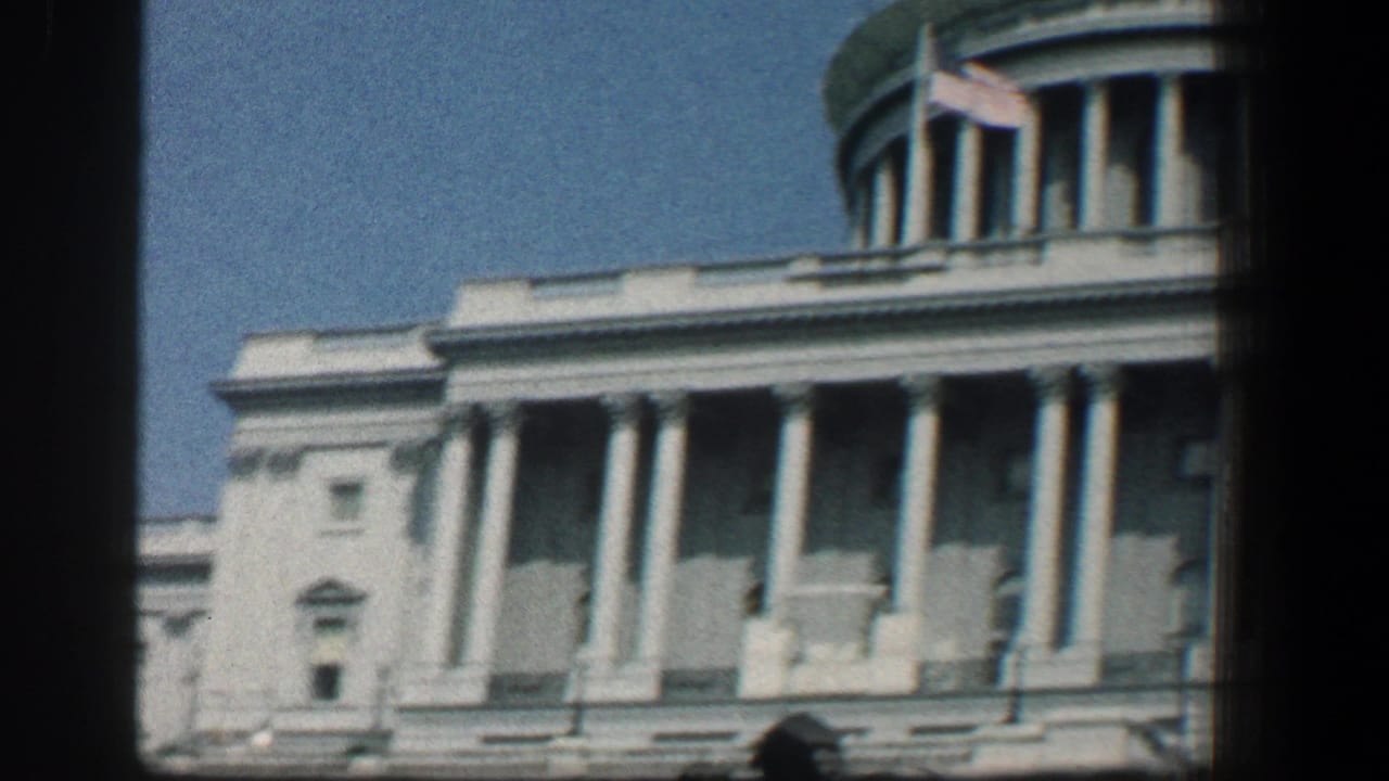 U.S. Capitol facade with columns, dome, flag, and dark film borders.