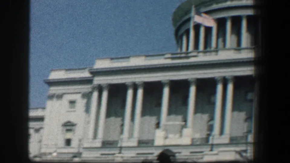 1961 8mm view of the U.S. Capitol facade, showing columns, part of the dome, an American flag, and dark film edges.