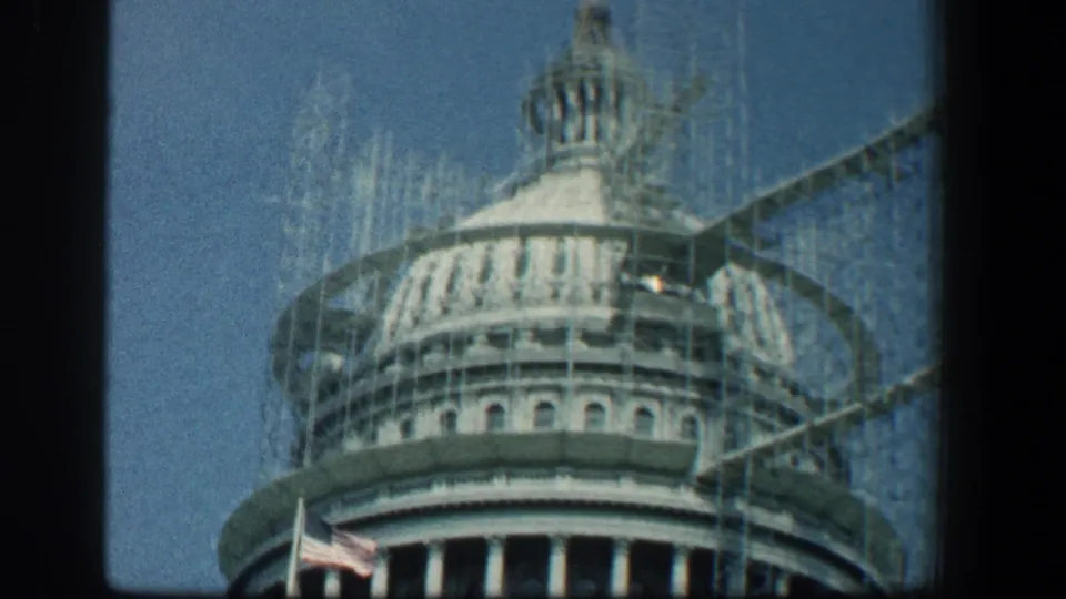Close 1961 8mm view of the Capitol dome encased in scaffolding, with an American flag below and dark film borders.