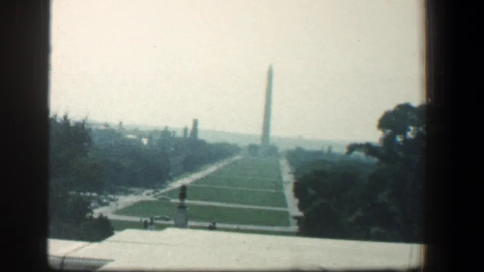1961 8mm wide view from near the Capitol grounds toward the Washington Monument, with lawn paths, trees, and tiny distant people.