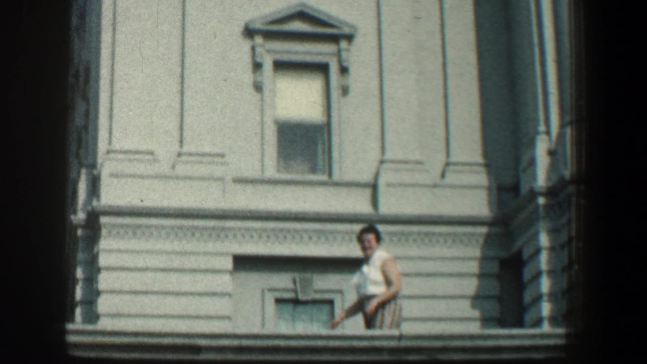 Woman in a white top stands near a pale classical building facade.