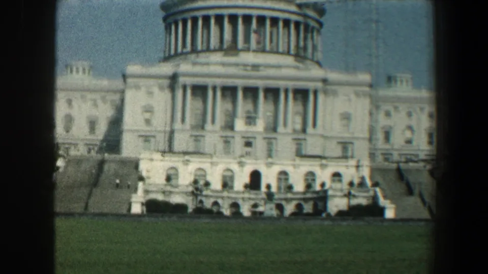 Wide 1961 8mm view of the U.S. Capitol across a green lawn, showing the dome, steps, columns, and soft color film texture.