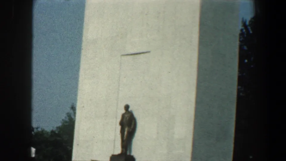 1961 8mm view near the Washington Monument base, with a statue in front and a small visitor visible nearby.