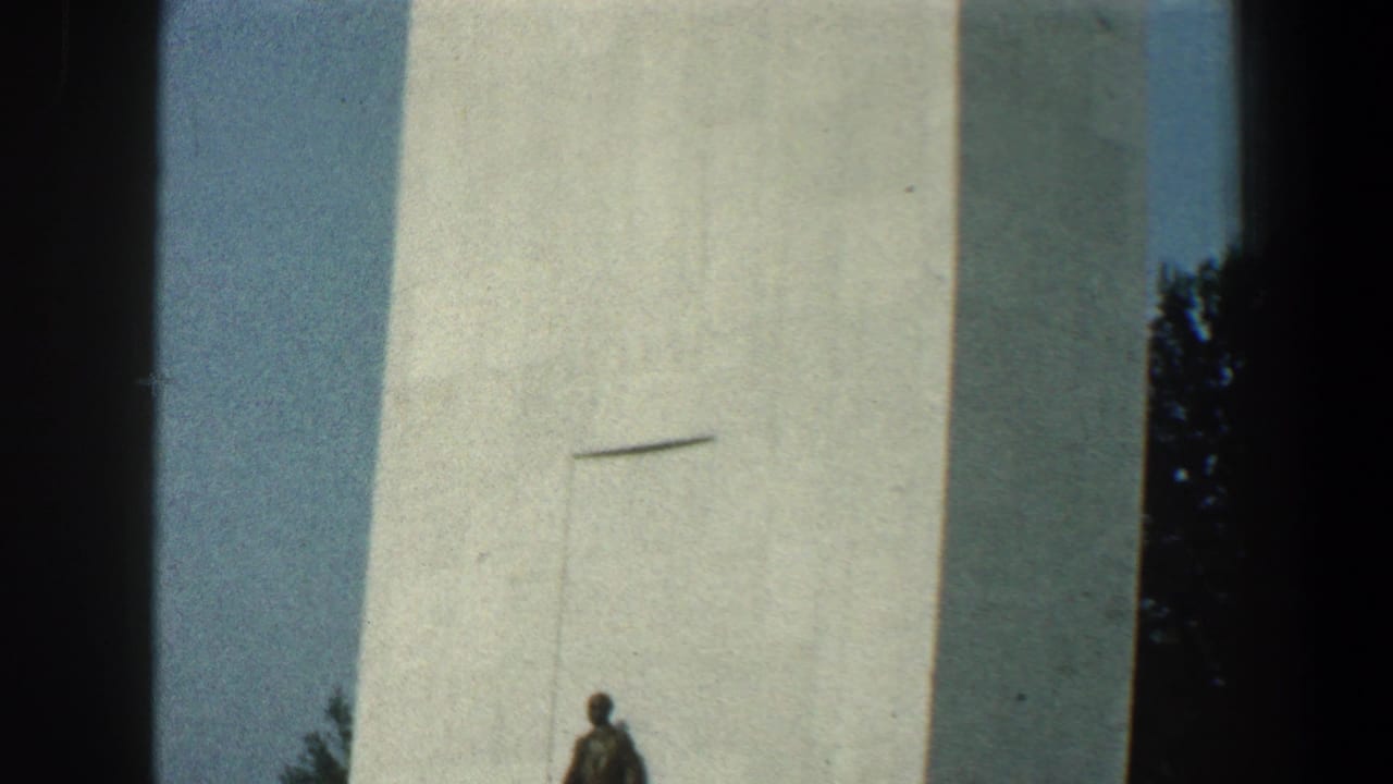 Tall white tower with a small statue or figure near its base against blue sky.