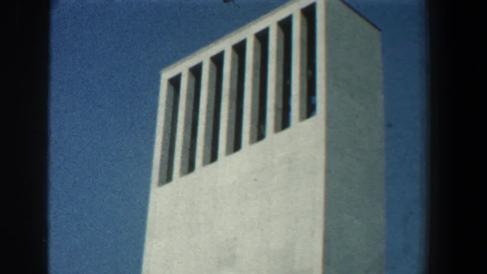 Close 1961 home-movie view of the tower's upper section, showing tall vertical slits and pale walls against blue sky.