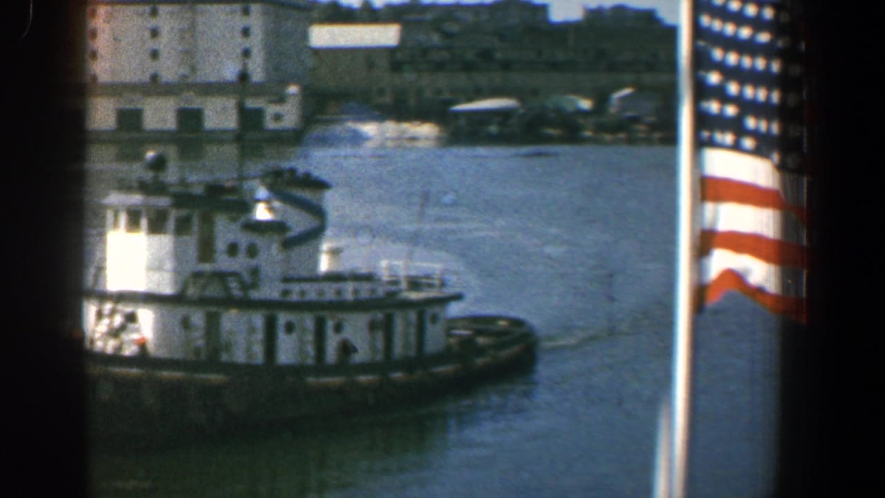 White tugboat on harbor water with part of an American flag at the right edge.