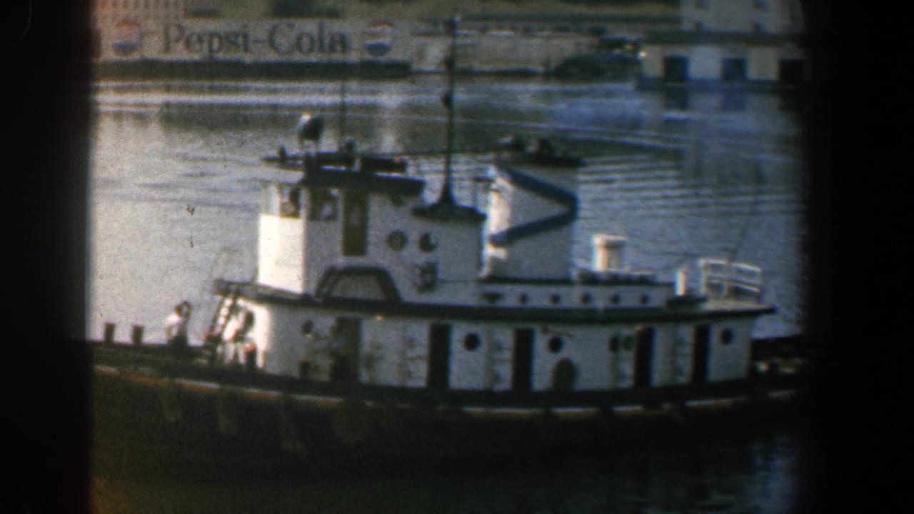 White tugboat on harbor water with crew visible and a Pepsi-Cola sign in the background.