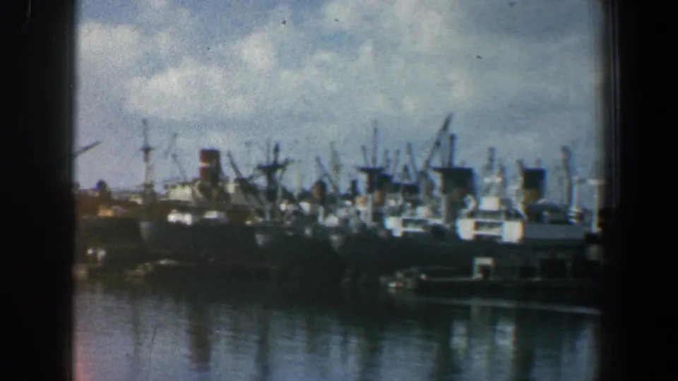 A dense Baltimore harbor scene shows docked ships, cranes, masts, and reflections on the water in soft 1961 8mm color.
