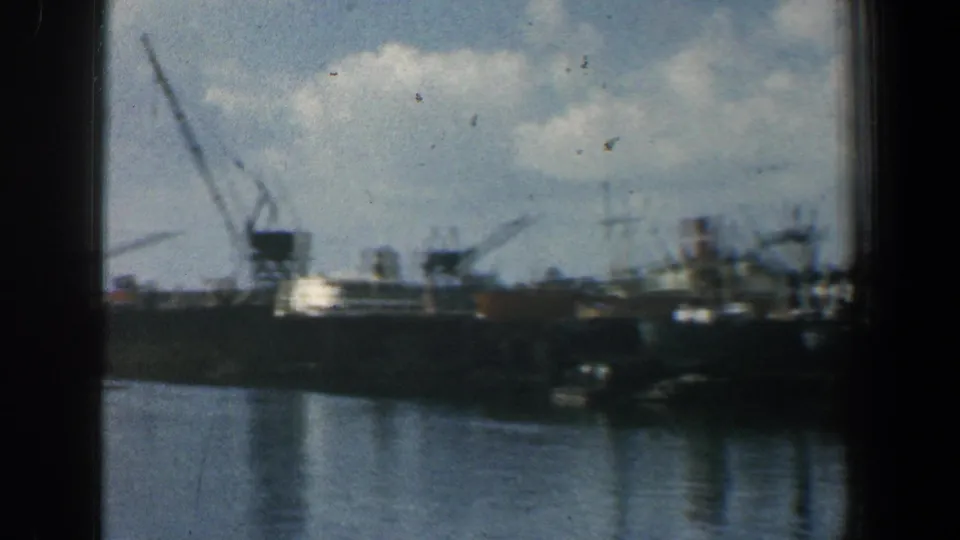 1961 Baltimore harbor view on 8mm film, showing docked ships, cranes, water, and a partly cloudy sky.