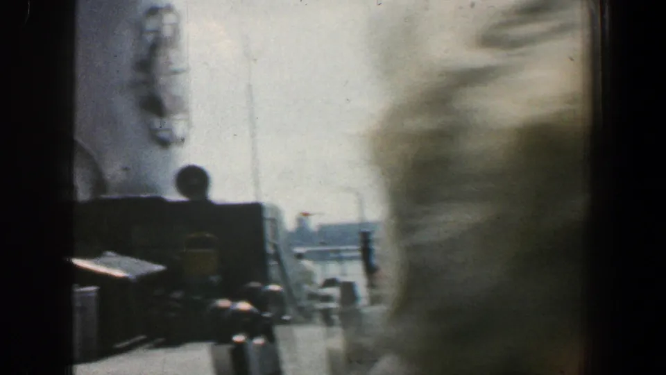 Baltimore harbor home-movie frame with a blurred passenger passing close to camera and ship deck structures behind.