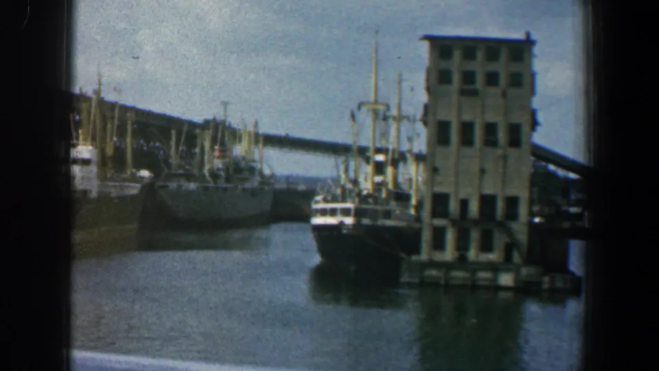 1961 Baltimore harbor view with large docked ships, a pier building, calm water, and visible 8mm frame edges.