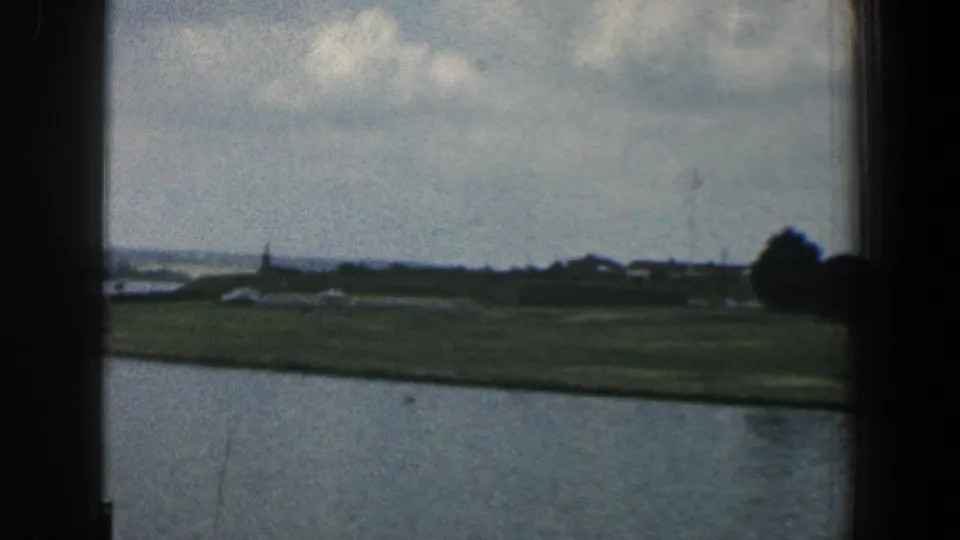 1961 Baltimore-area frame showing a broad river foreground and a low shoreline with trees and small structures in the distance.
