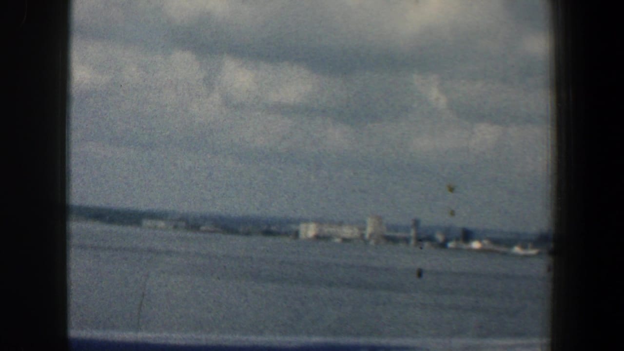 Window-framed view across open water toward a distant shoreline and pale city buildings.
