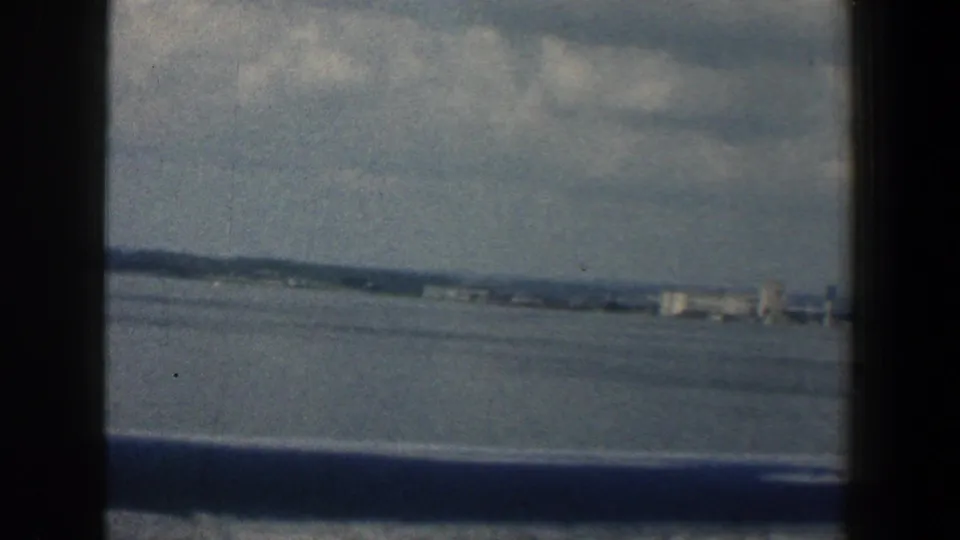 1961 Baltimore-area 8mm frame with open water, distant low buildings, hazy horizon, and dark vessel window edges.
