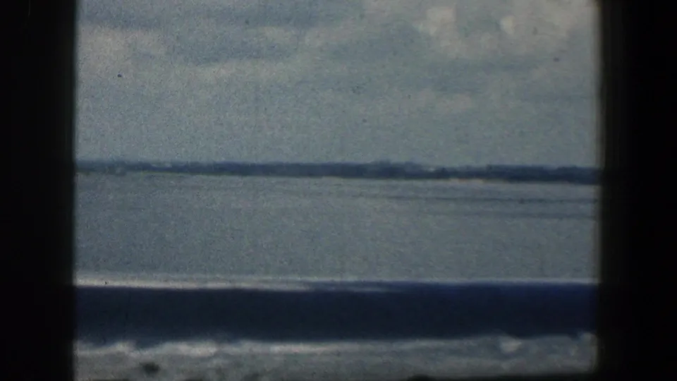 Muted 8mm frame showing Baltimore-area water and a distant shore through a dark central divider and lower band.