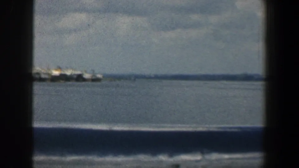 1961 Baltimore-area waterfront frame with several distant boats clustered near the horizon under a cloudy sky.