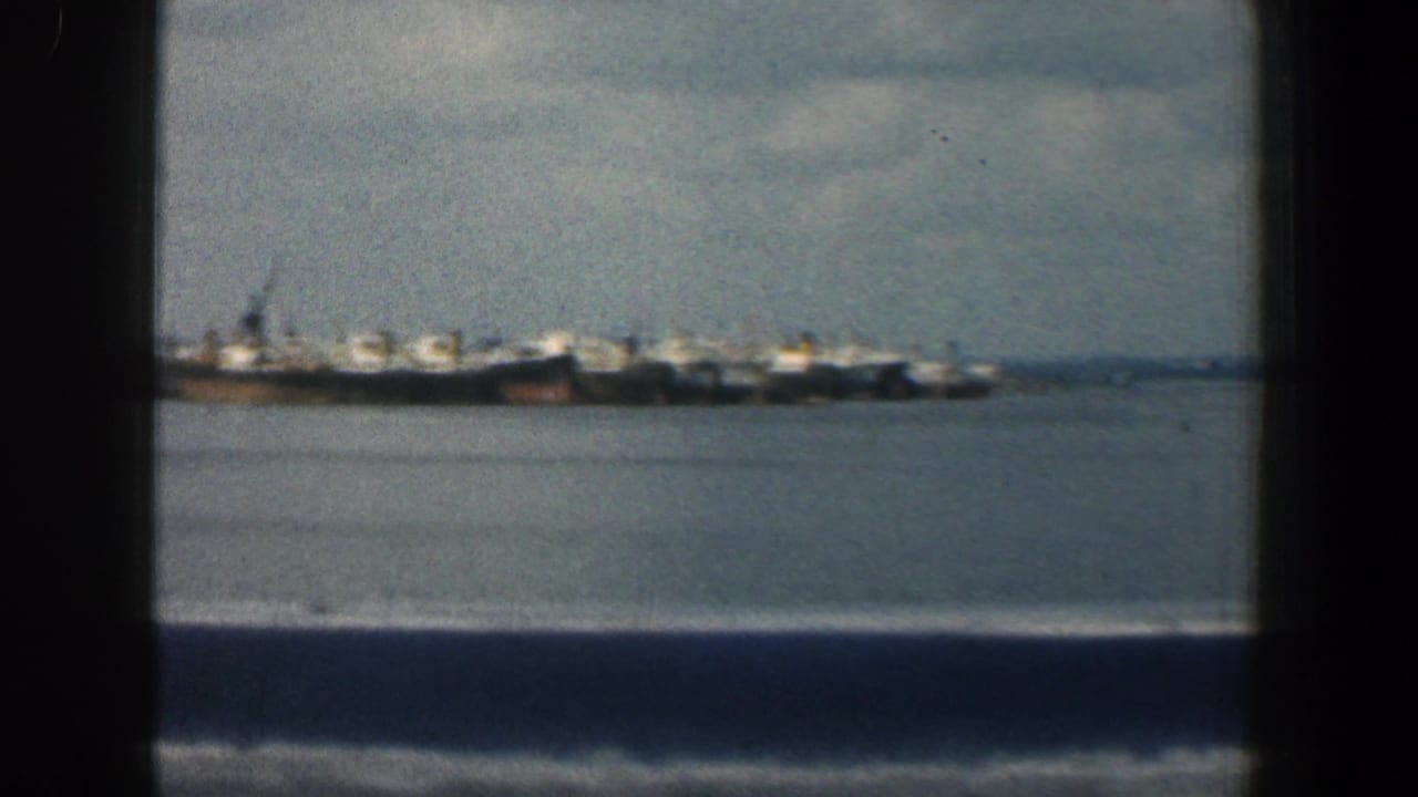 1961 Baltimore harbor view with distant docked ships across the water, filmed in soft color from a moving vessel.