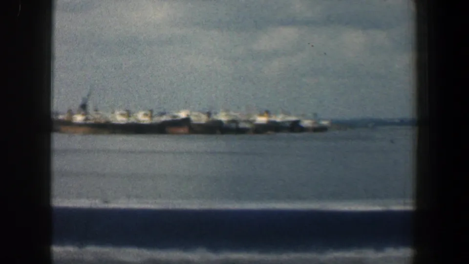 1961 Baltimore harbor view with distant docked ships across the water, filmed in soft color from a moving vessel.