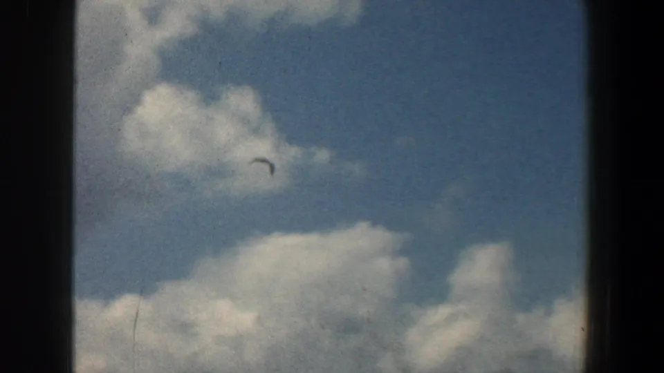 A small bird crosses a blue, cloud-filled sky in 1961 8mm home-movie footage from the Baltimore, Maryland metadata context.
