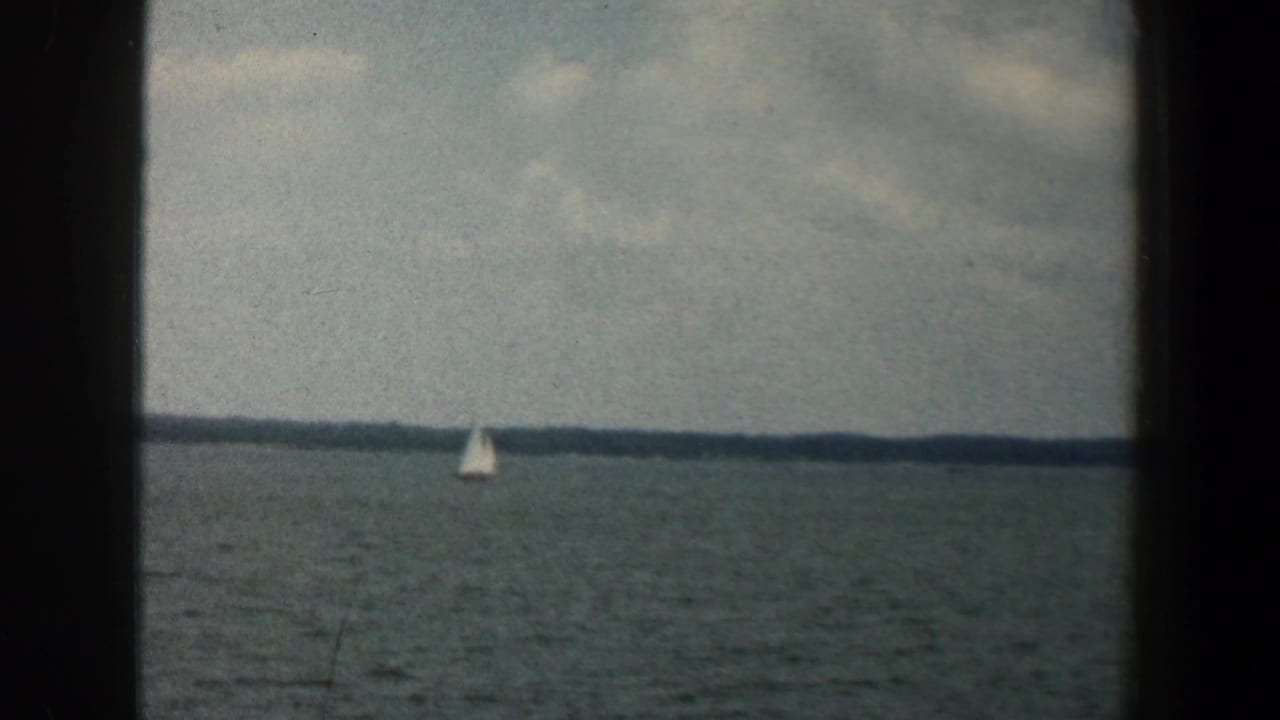 Small white sailboat on a lake beneath a cloudy sky.