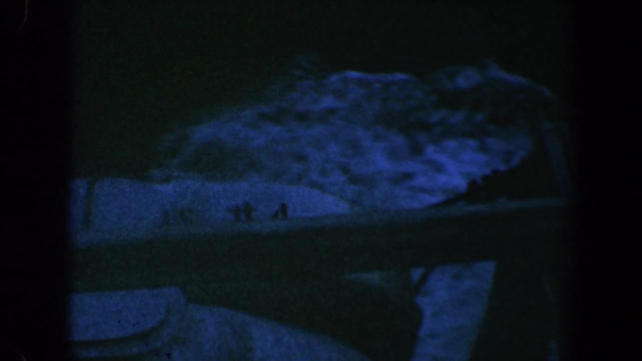 Blue-green nighttime view with a pale boat- or shoreline-like shape near water.