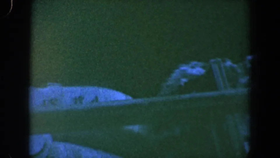Grainy 1961 Baltimore home-movie frame with an indistinct pale horizontal form, dark water tones, and soft reflected shapes.