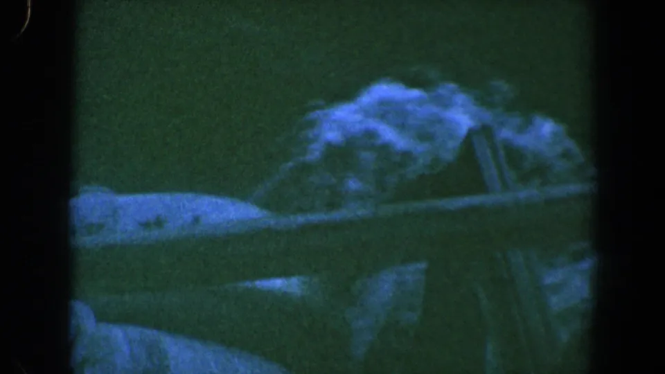 A dark 1961 8mm Baltimore frame showing a soft pale boat- or shoreline-like form above darker water reflections.
