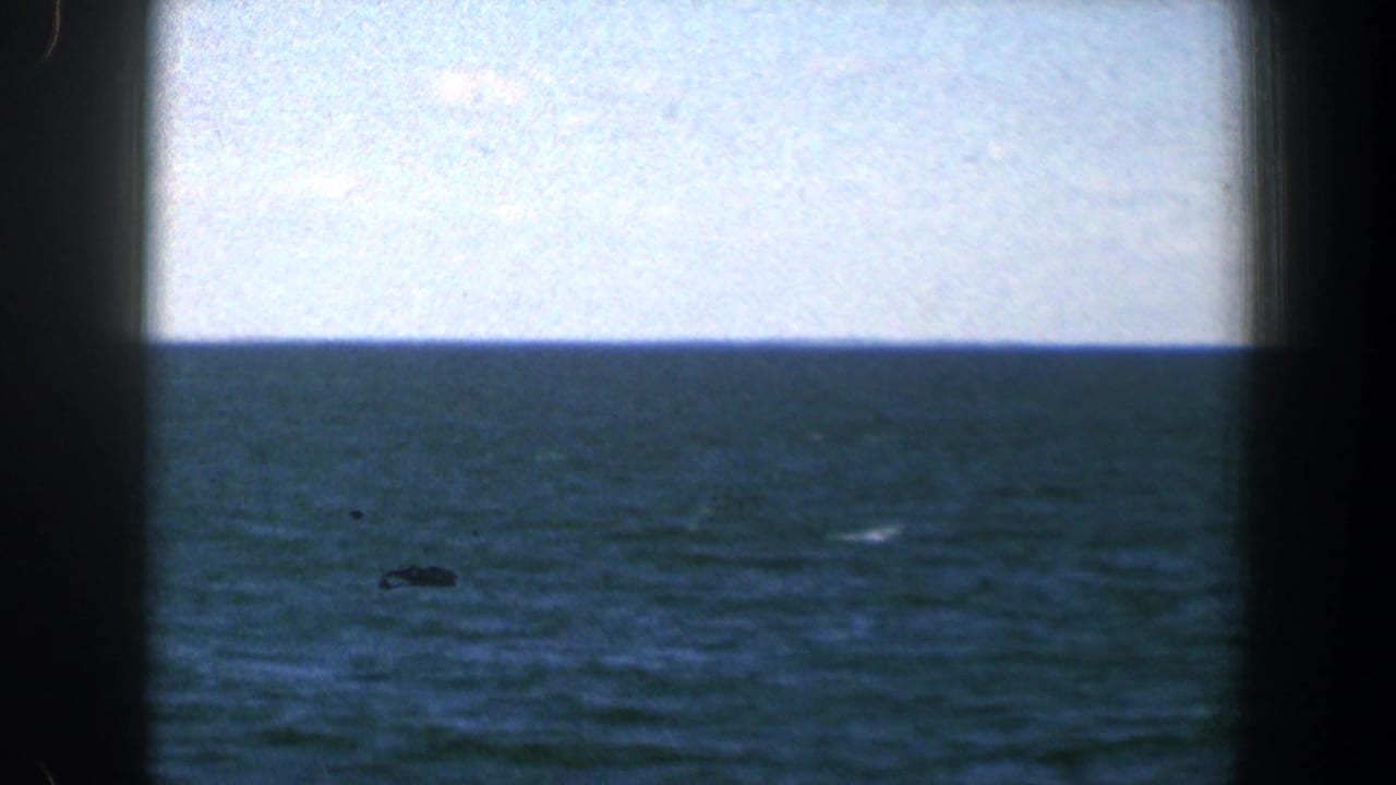 Blue-green water and pale sky seen through dark boat-window edges.