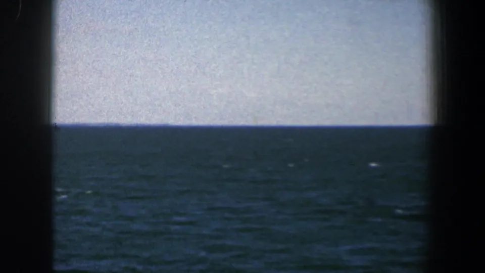 Blue sea and pale sky in a 1961 8mm Baltimore-area boat view, split by a dark vertical frame edge.