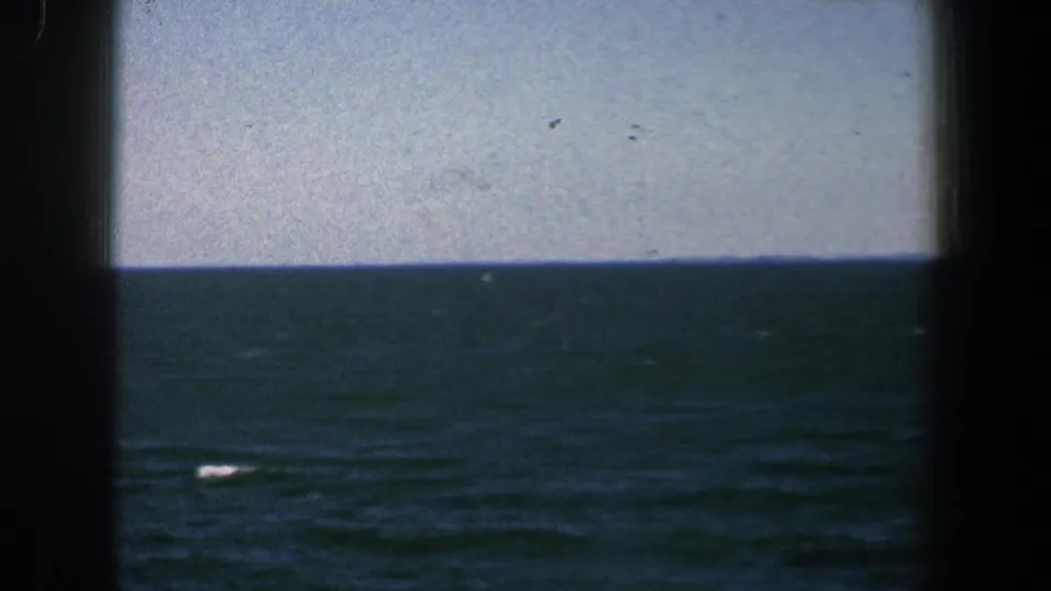 8mm frame of blue-green water near Baltimore with dark boat framing and a small white object low in the scene.