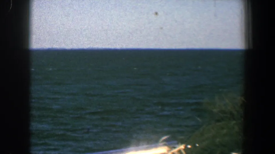 1961 8mm boat-view frame near Baltimore showing open water, horizon, dark framing, and a bright railing or deck edge.