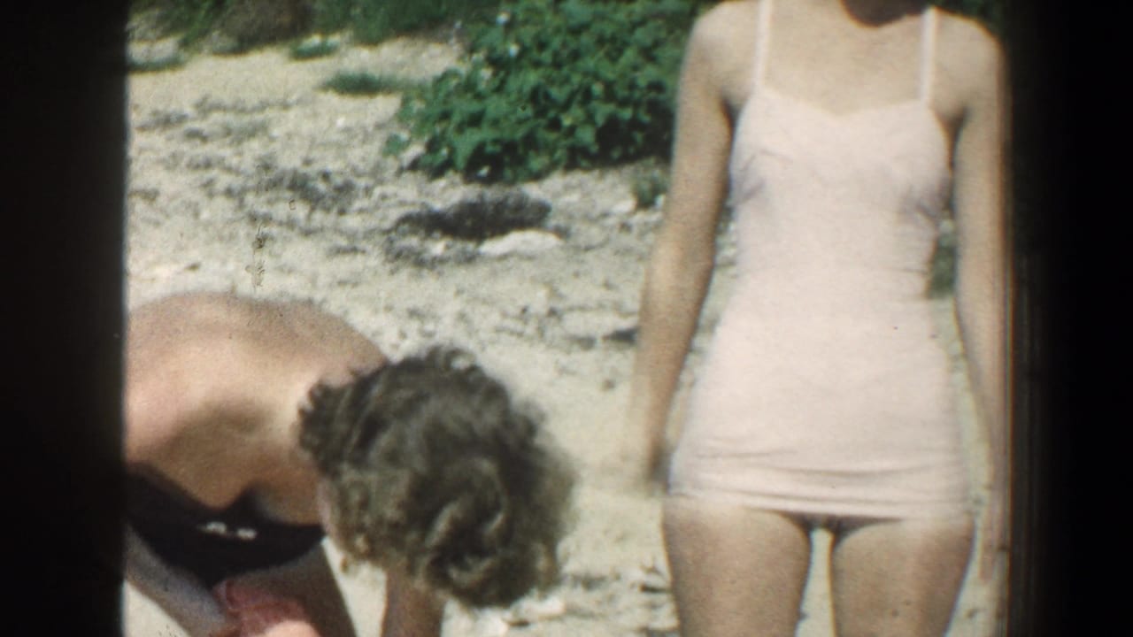 Person bends over with an orange towel beside a standing woman in a pink swimsuit.