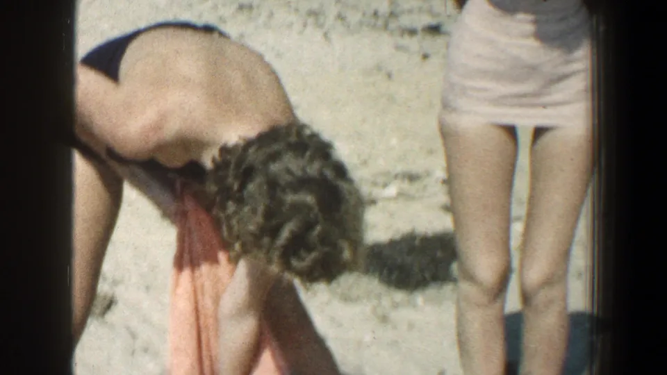 The beach scene shows a curly-haired person bending over an orange towel with the pink-swimsuit figure partly cropped nearby.