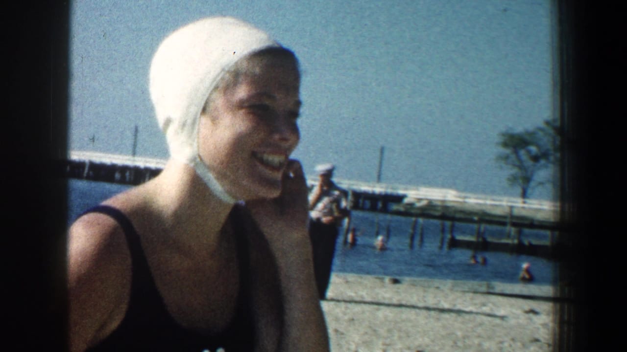 In supplied 1961 Baltimore beach footage, a woman in a white swim cap laughs beside the water with a distant pier behind her.