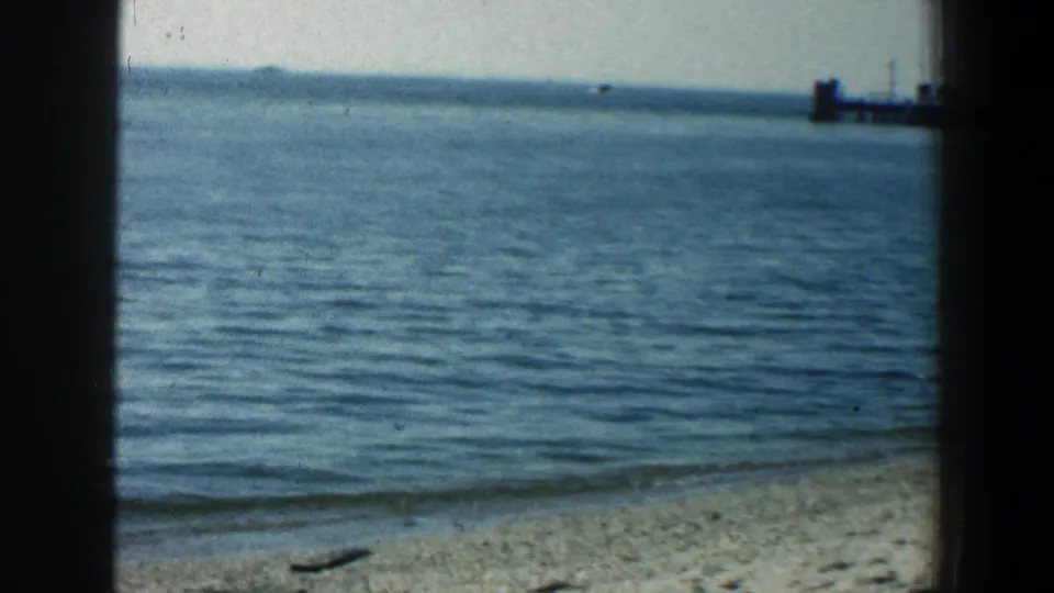 The beach shoreline and calm water appear in the supplied 1961 Baltimore footage, with a distant pier partly visible to the right.