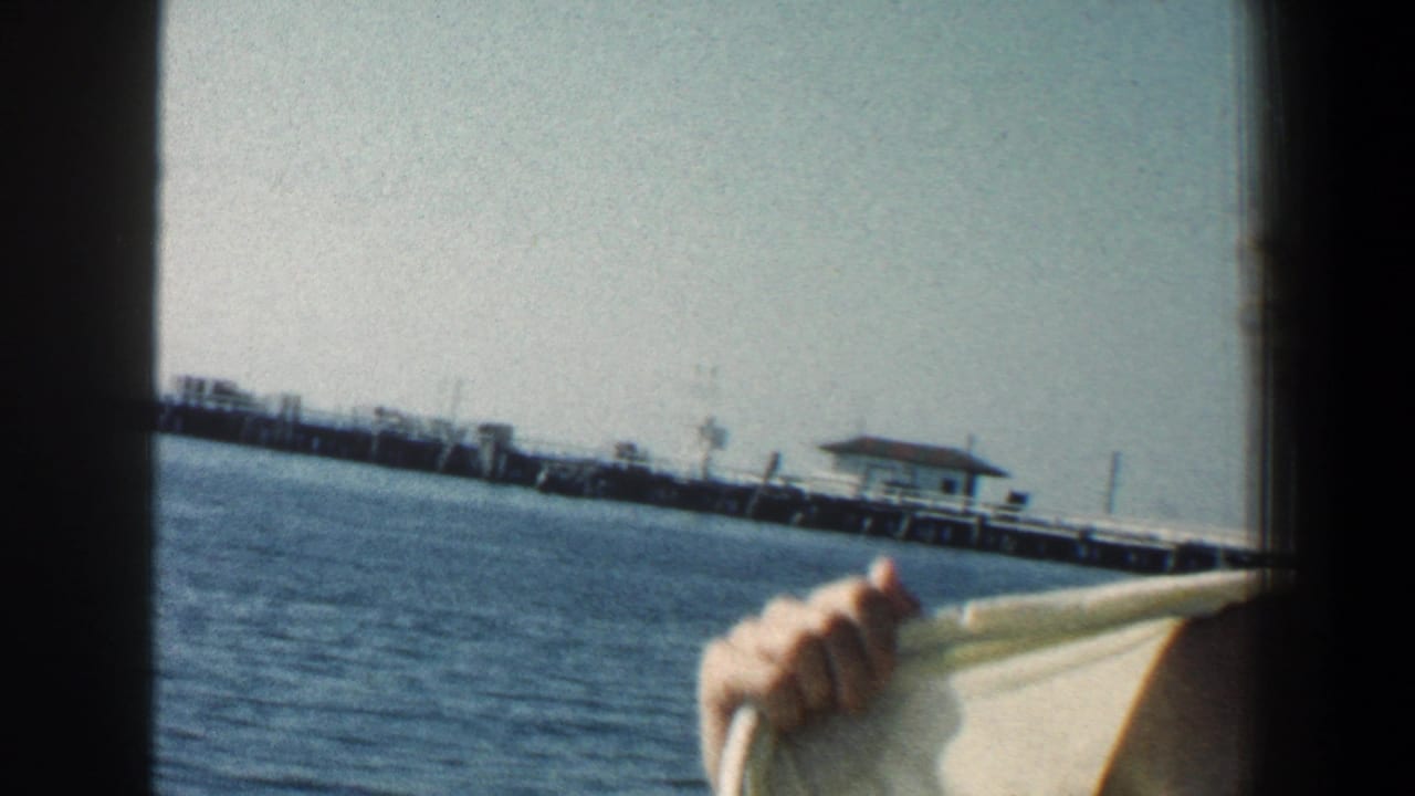 Distant pier across blue water with a partial arm and cloth near the camera.