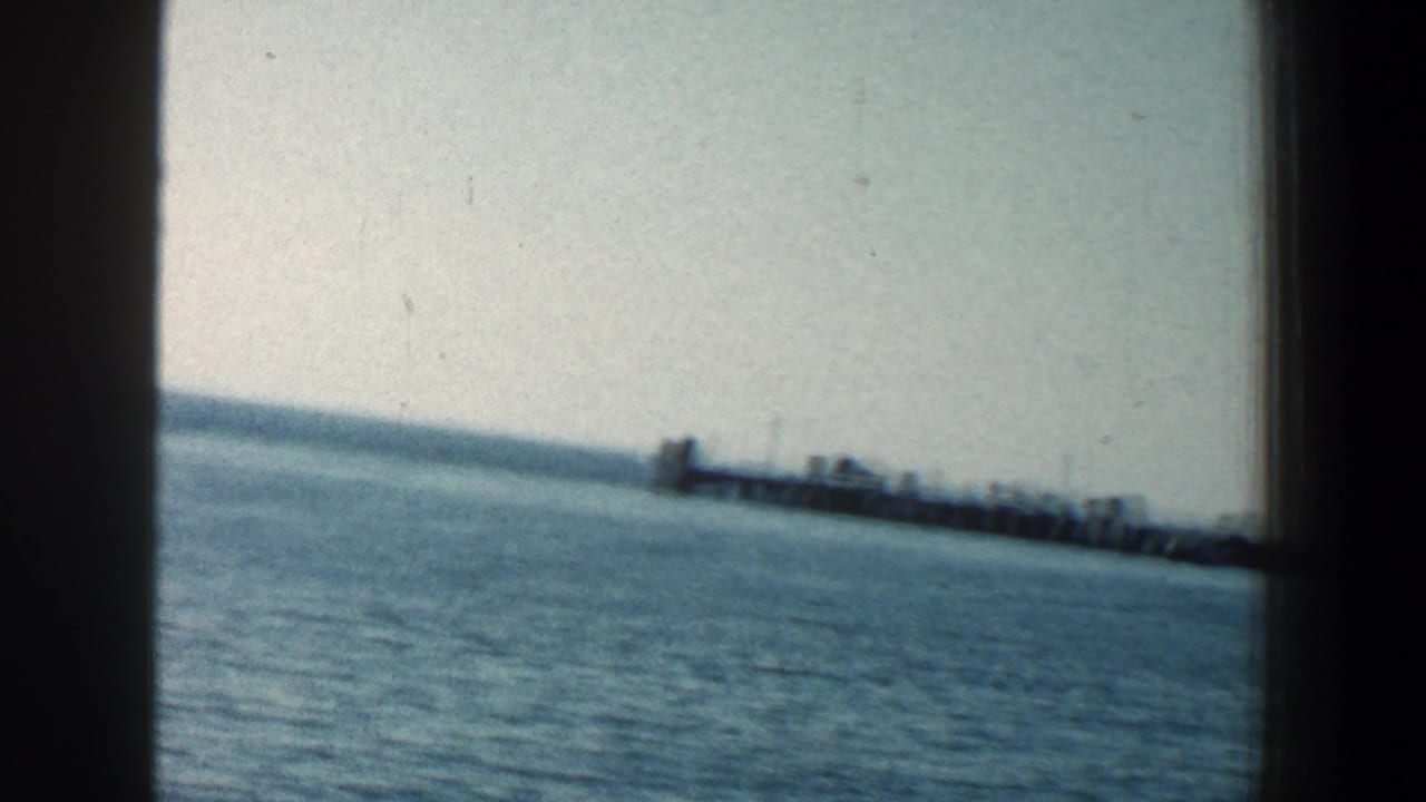Blue water and sandy shoreline with a distant pier near the horizon.